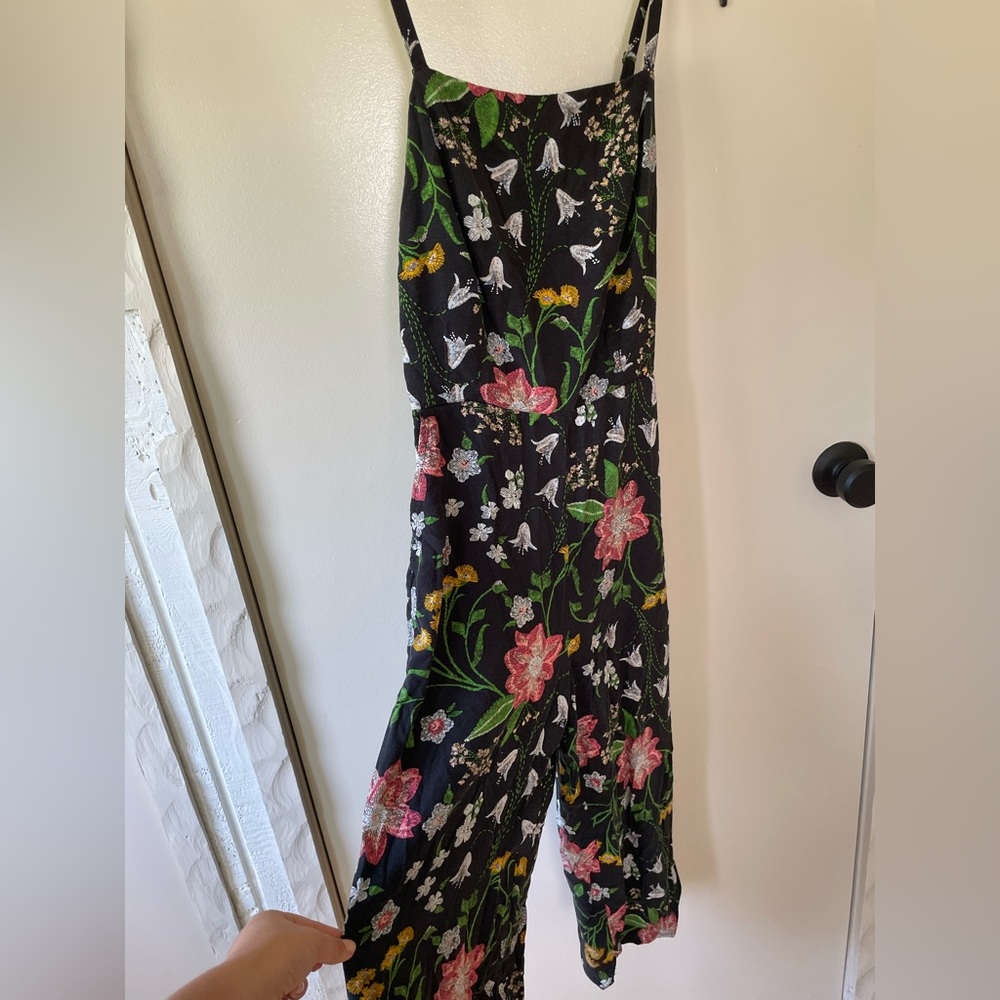 Black floral romper with a fitted high neck and wide leg pants.